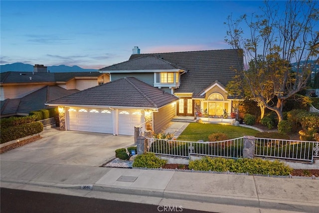 traditional home featuring an attached garage, a tile roof, concrete driveway, and a fenced front yard