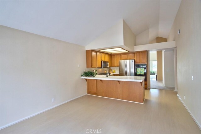 kitchen featuring stainless steel appliances, light countertops, light wood-style floors, a peninsula, and high vaulted ceiling