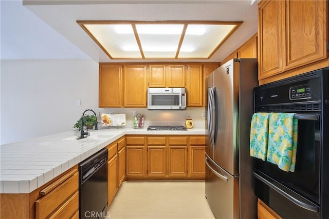 kitchen featuring brown cabinets, a sink, a warming drawer, black appliances, and a peninsula