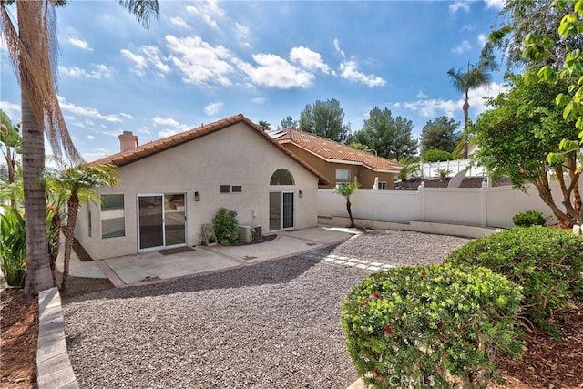 back of house featuring a tiled roof, a chimney, cooling unit, and stucco siding