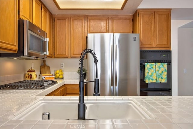 kitchen with brown cabinetry, appliances with stainless steel finishes, tile countertops, and a sink