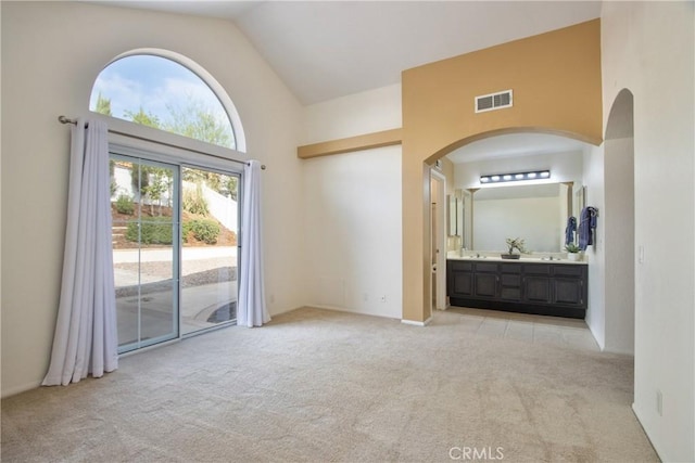 unfurnished bedroom with access to exterior, visible vents, light carpet, arched walkways, and high vaulted ceiling