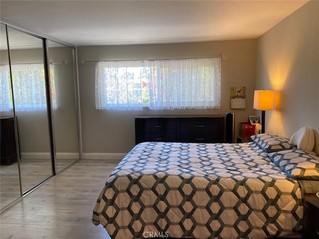 bedroom with wood finished floors, baseboards, a closet, and multiple windows