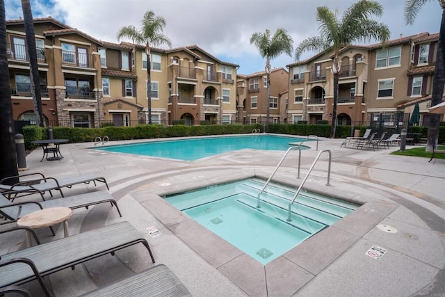 pool with a patio area, a community hot tub, and fence