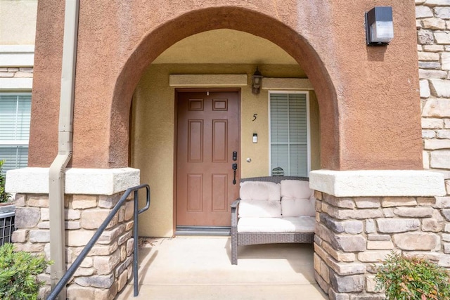 entrance to property with stone siding, covered porch, and stucco siding