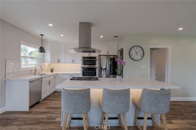 kitchen with island exhaust hood, a sink, tasteful backsplash, white cabinetry, and appliances with stainless steel finishes
