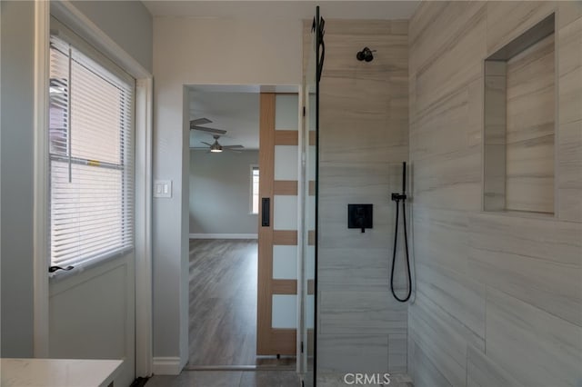 full bath featuring baseboards, vanity, ceiling fan, and tiled shower