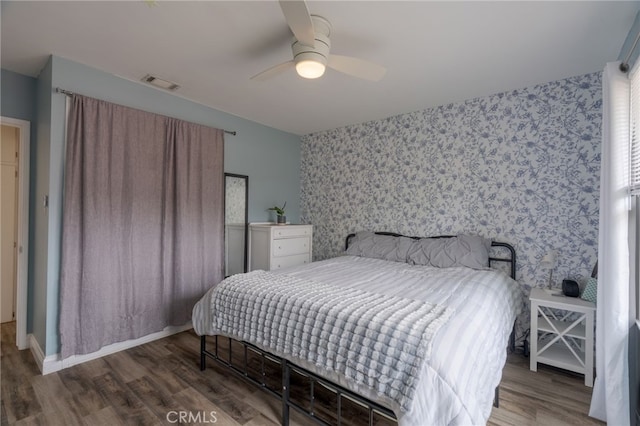 bedroom with wallpapered walls, wood finished floors, visible vents, baseboards, and ceiling fan