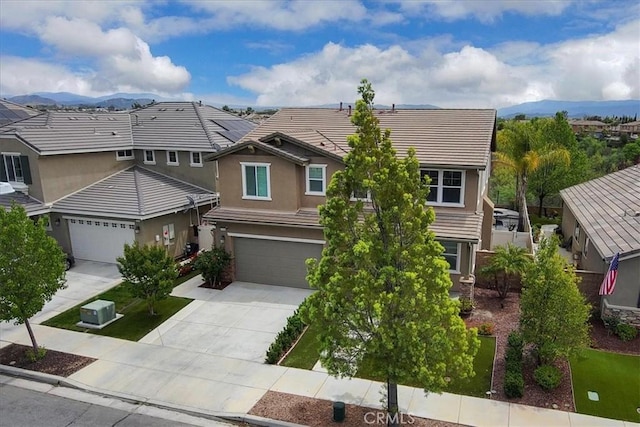 view of front facade with a mountain view, a tiled roof, a garage, concrete driveway, and stucco siding