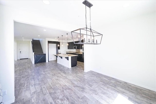kitchen featuring open floor plan, stainless steel microwave, an island with sink, and wood finished floors
