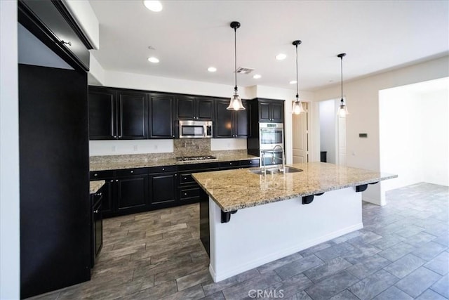 kitchen featuring a sink, appliances with stainless steel finishes, a breakfast bar, dark cabinetry, and recessed lighting