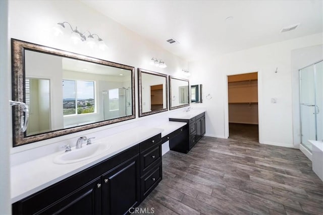full bath with vanity, a stall shower, a walk in closet, visible vents, and wood finished floors