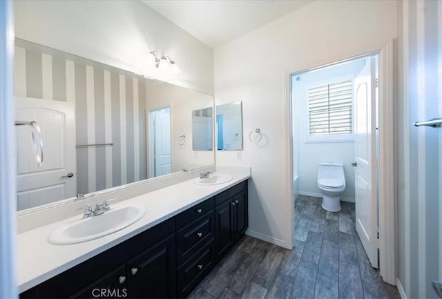 full bath featuring wood finished floors, double vanity, a sink, and baseboards