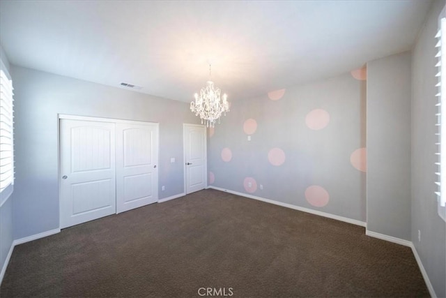 carpeted empty room featuring a notable chandelier, visible vents, and baseboards