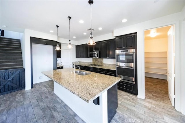 kitchen with a large island with sink, light stone countertops, light wood-type flooring, a sink, and stainless steel appliances