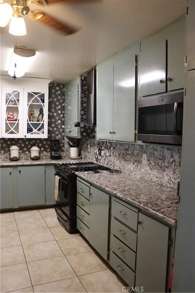 216 Barros St, Patterson, CA 95363 - kitchen with wall chimney range hood, light tile patterned flooring, stainless steel microwave, backsplash, and black gas range oven