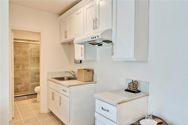 kitchen with white cabinets, a sink, light countertops, under cabinet range hood, and light tile patterned floors