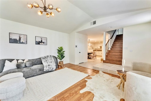 living area featuring stairway, light wood-type flooring, an inviting chandelier, lofted ceiling, and visible vents