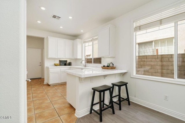 kitchen with visible vents, a healthy amount of sunlight, a breakfast bar area, tile counters, and white cabinets