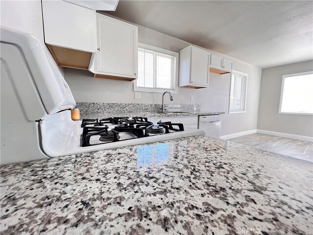 kitchen featuring white cabinets, a sink, a healthy amount of sunlight, light stone countertops, and dishwasher