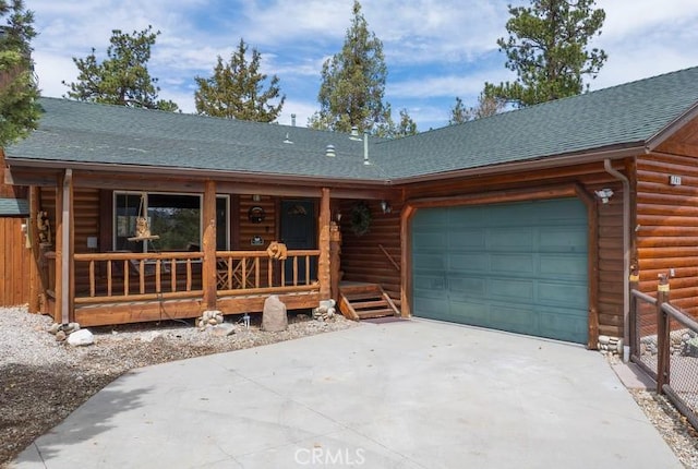 cabin with driveway, covered porch, an attached garage, faux log siding, and roof with shingles