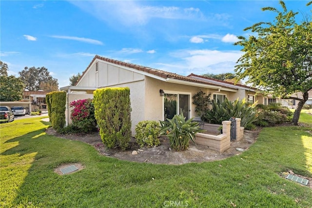 view of side of property with a lawn, a tile roof, and stucco siding