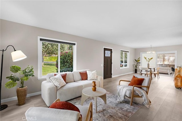 living area with baseboards, an inviting chandelier, and light wood-style flooring