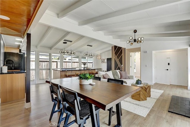 dining area with baseboards, light wood finished floors, lofted ceiling with beams, and a notable chandelier