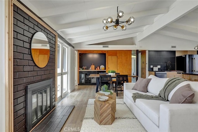 living area with lofted ceiling with beams, a brick fireplace, an inviting chandelier, and light wood-type flooring