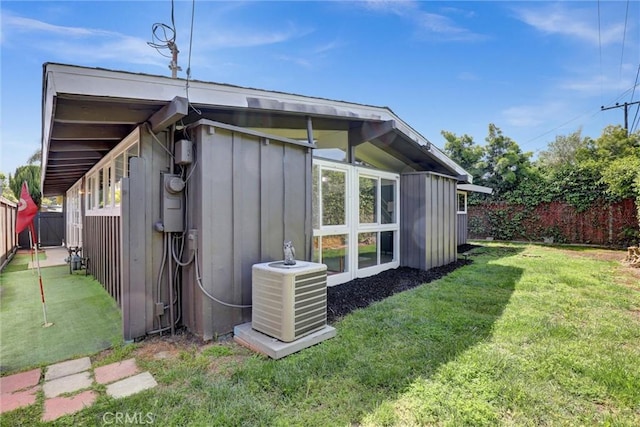 view of home's exterior featuring board and batten siding, a fenced backyard, a yard, and central AC