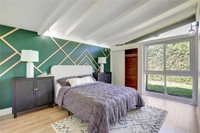 bedroom featuring vaulted ceiling with beams, wood finished floors, an accent wall, and a closet