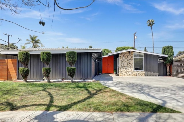 mid-century home with board and batten siding, driveway, stone siding, and a front yard