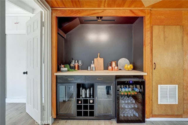 bar featuring wood finished floors, visible vents, beverage cooler, and a bar