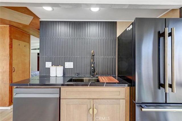 kitchen featuring recessed lighting, dark countertops, light brown cabinets, a sink, and freestanding refrigerator