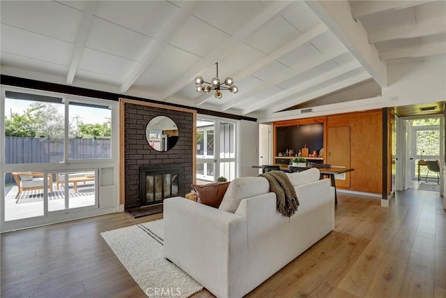 living room with lofted ceiling with beams, a brick fireplace, a chandelier, and light wood-type flooring