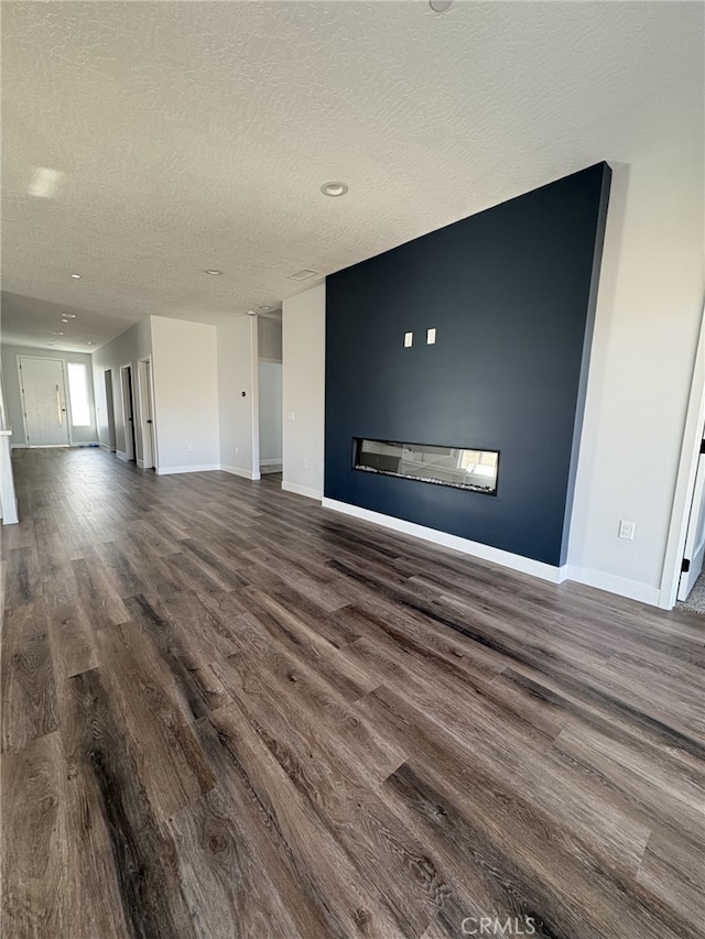 12525 Spring Valley Pkwy, Victorville, CA 92395 - unfurnished living room with dark wood finished floors, baseboards, a glass covered fireplace, and a textured ceiling