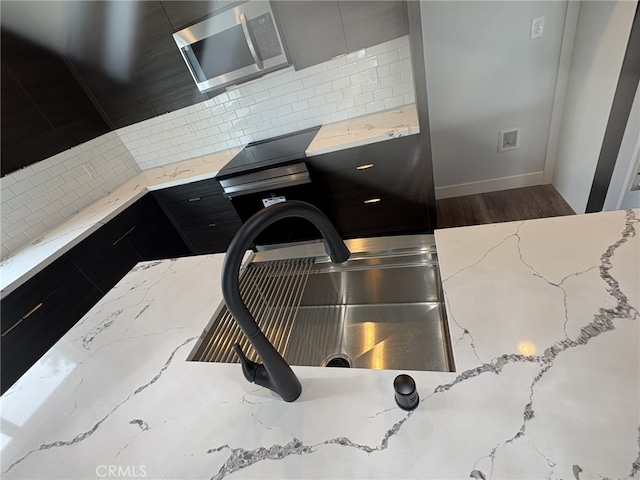12525 Spring Valley Pkwy, Victorville, CA 92395 - room details featuring tasteful backsplash, wood finished floors, stainless steel microwave, dark cabinets, and light stone countertops