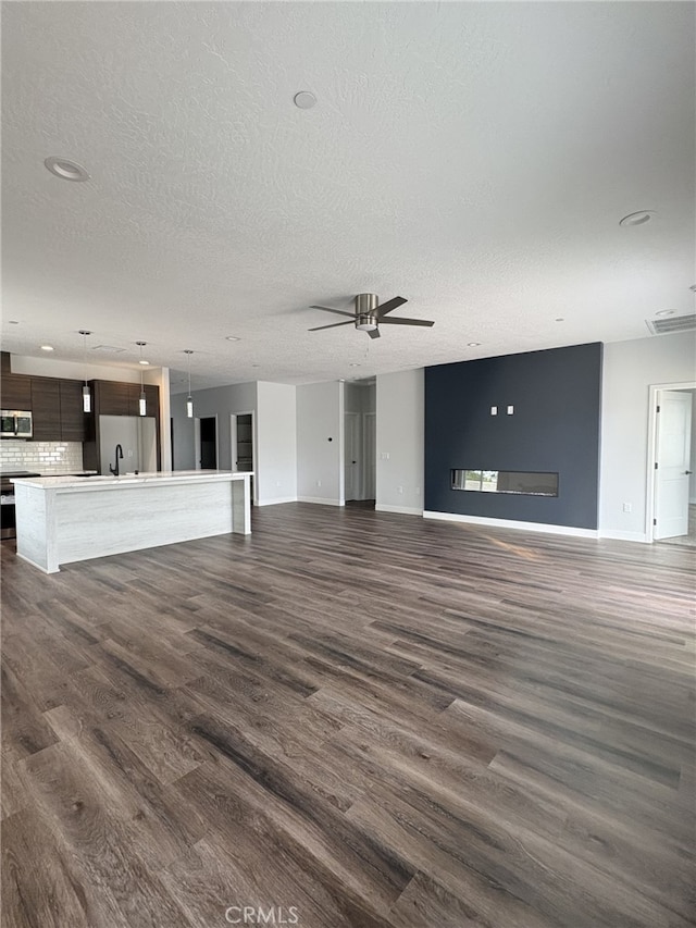 12525 Spring Valley Pkwy, Victorville, CA 92395 - unfurnished living room featuring a sink, a textured ceiling, ceiling fan, dark wood finished floors, and baseboards