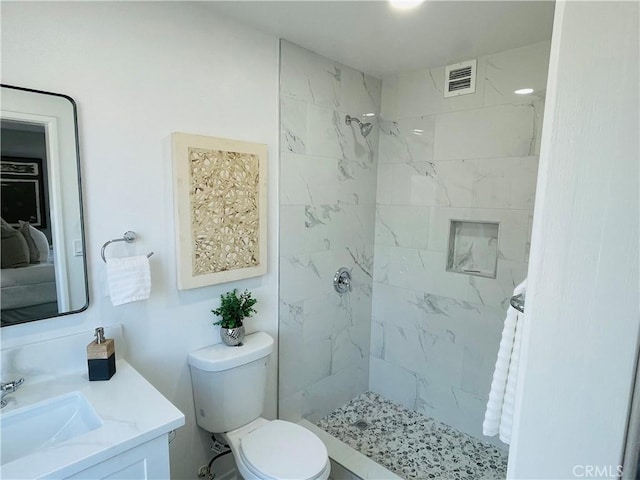 bathroom with a tile shower, toilet, vanity, and visible vents