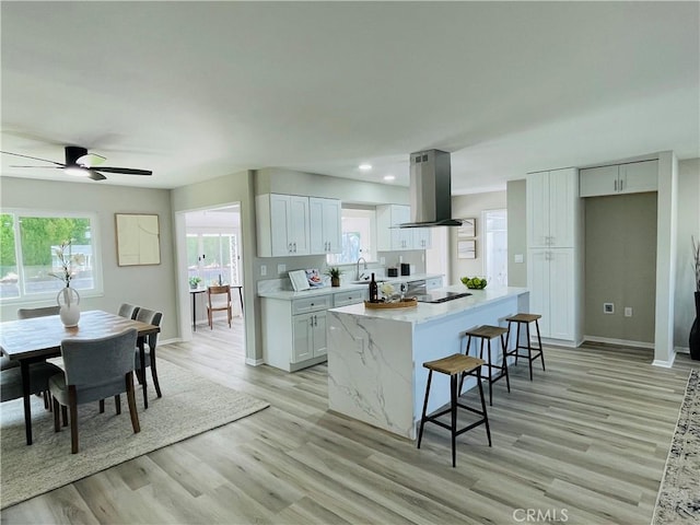 kitchen with white cabinets, island range hood, a sink, a kitchen island, and a kitchen bar