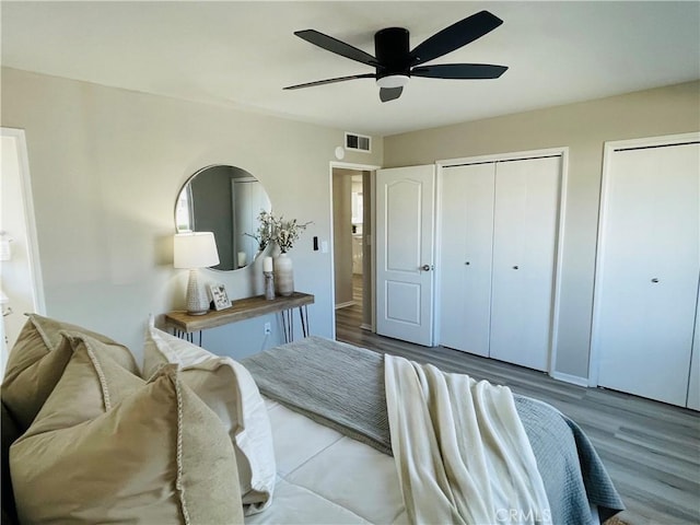 bedroom featuring ceiling fan, wood finished floors, visible vents, and two closets