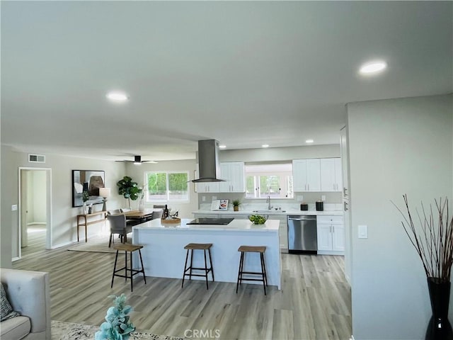 kitchen featuring light wood-style flooring, a sink, island range hood, dishwasher, and a breakfast bar