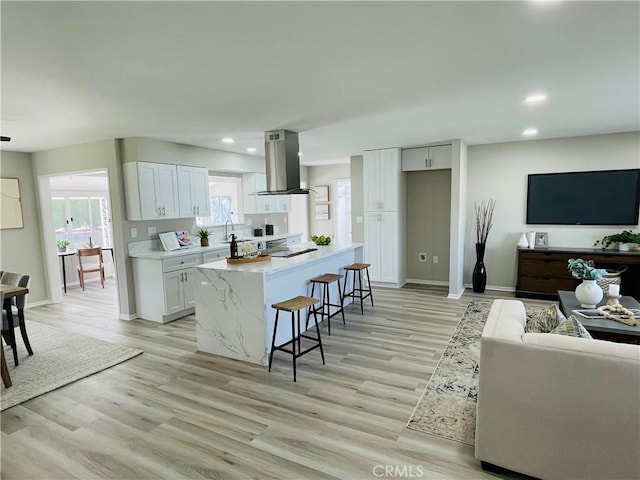 kitchen featuring baseboards, recessed lighting, white cabinetry, island range hood, and a breakfast bar area