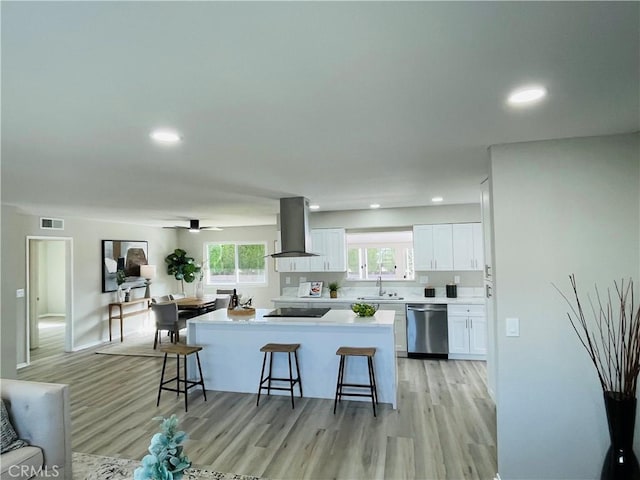 kitchen featuring stainless steel dishwasher, a center island, a sink, island range hood, and a breakfast bar area