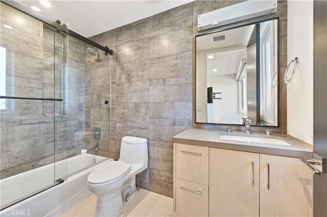 bathroom with combined bath / shower with glass door, toilet, vanity, visible vents, and tile walls