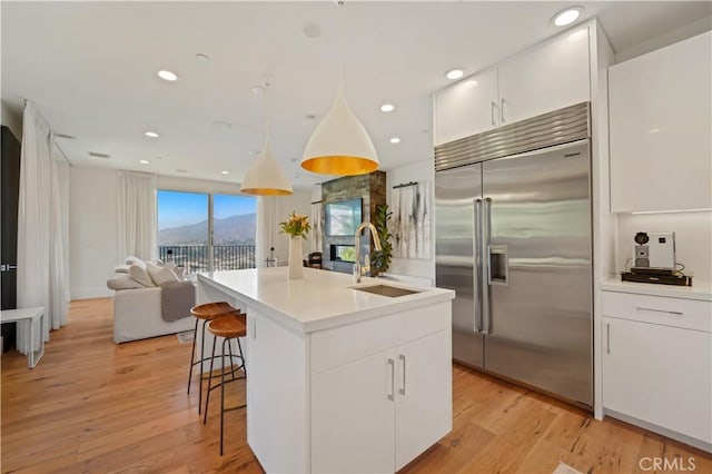 kitchen with a sink, open floor plan, an island with sink, stainless steel built in refrigerator, and white cabinetry