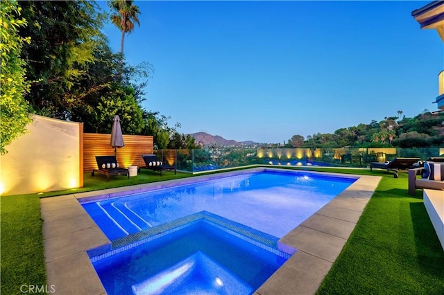 outdoor pool with a lawn, fence, a mountain view, and an in ground hot tub
