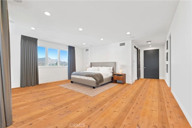 bedroom with recessed lighting, a barn door, baseboards, and light wood-style flooring