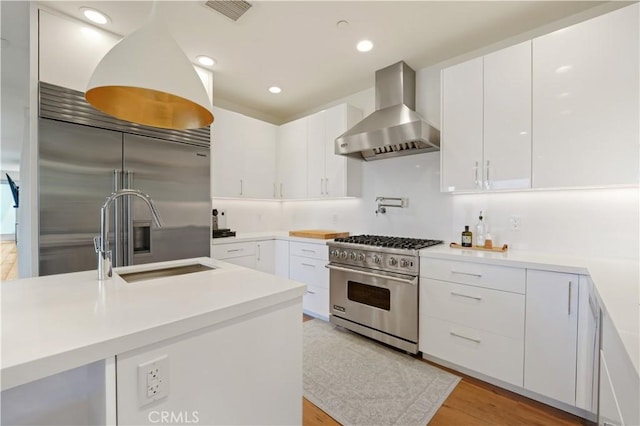 kitchen with wall chimney range hood, high quality appliances, visible vents, and white cabinets