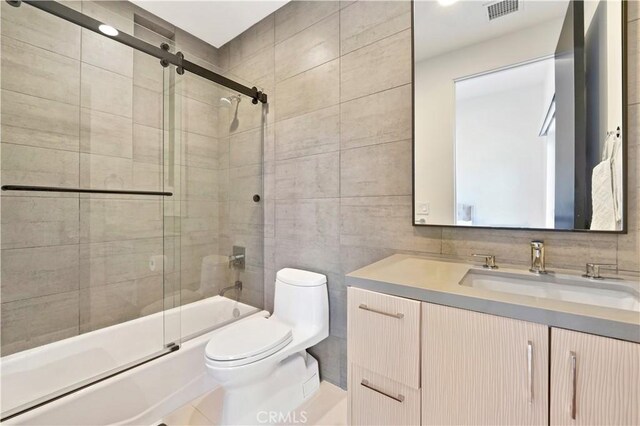 bathroom with toilet, tile walls, visible vents, vanity, and enclosed tub / shower combo